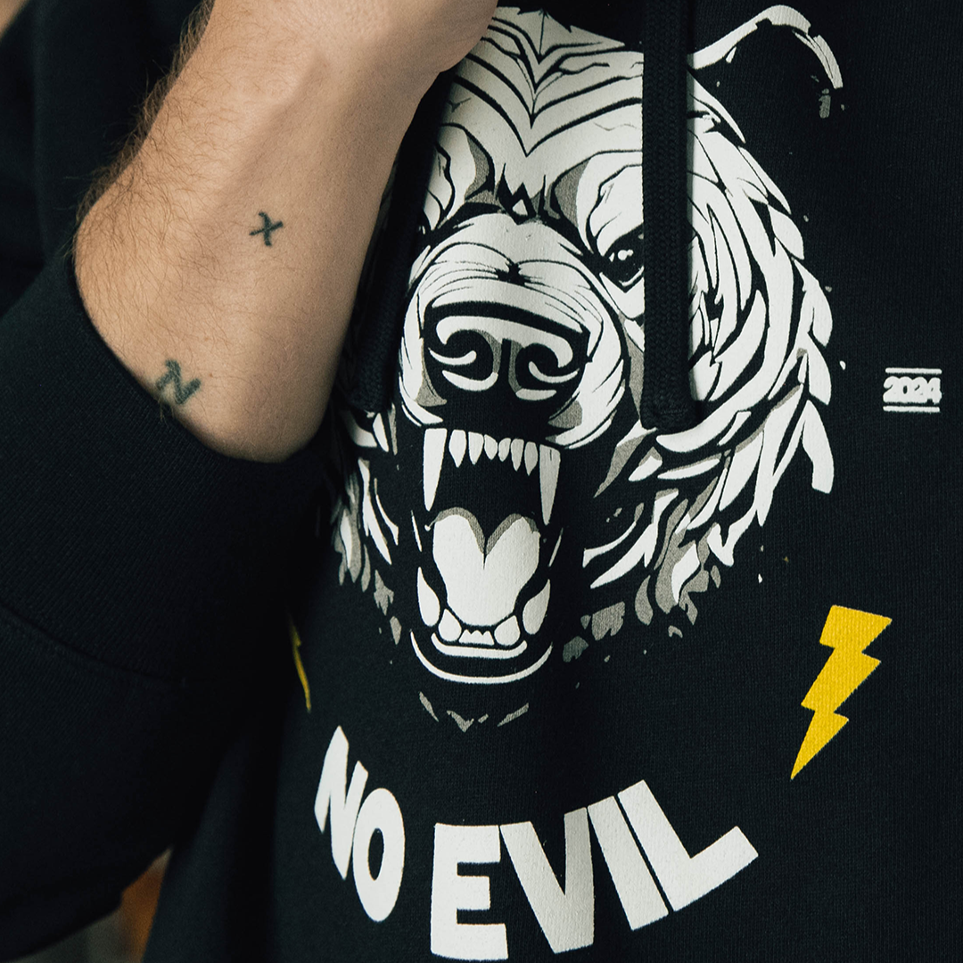 A close up photo of a man with arm tattoos wearing the fear no evil bear hoodie