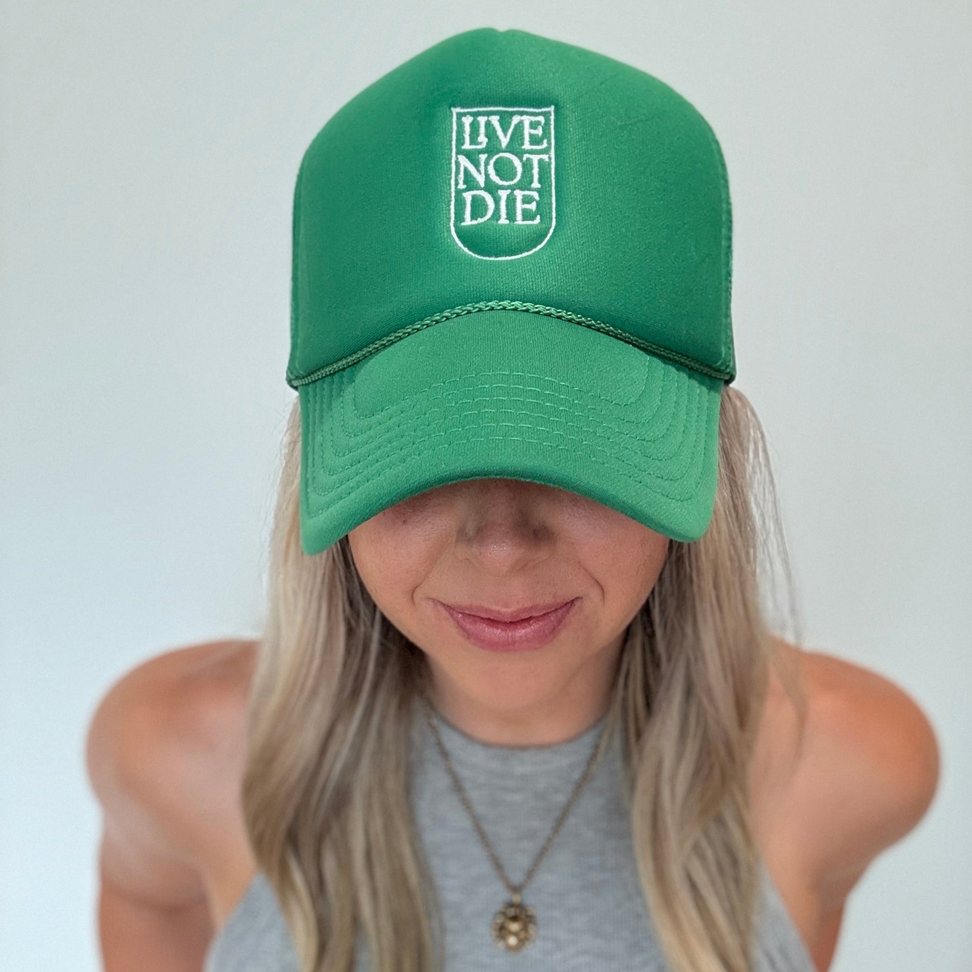 Person wearing a green cap with 'Live Not Die' text on a plain background